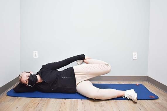 Person ligger på sidan på en yogamatta och stretchar höften